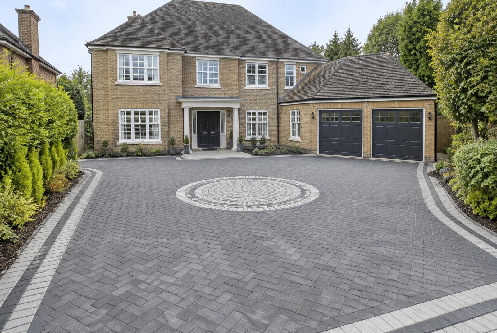 Large charcoal block paved driveway with pale contrasting border and circular feature at a detached house